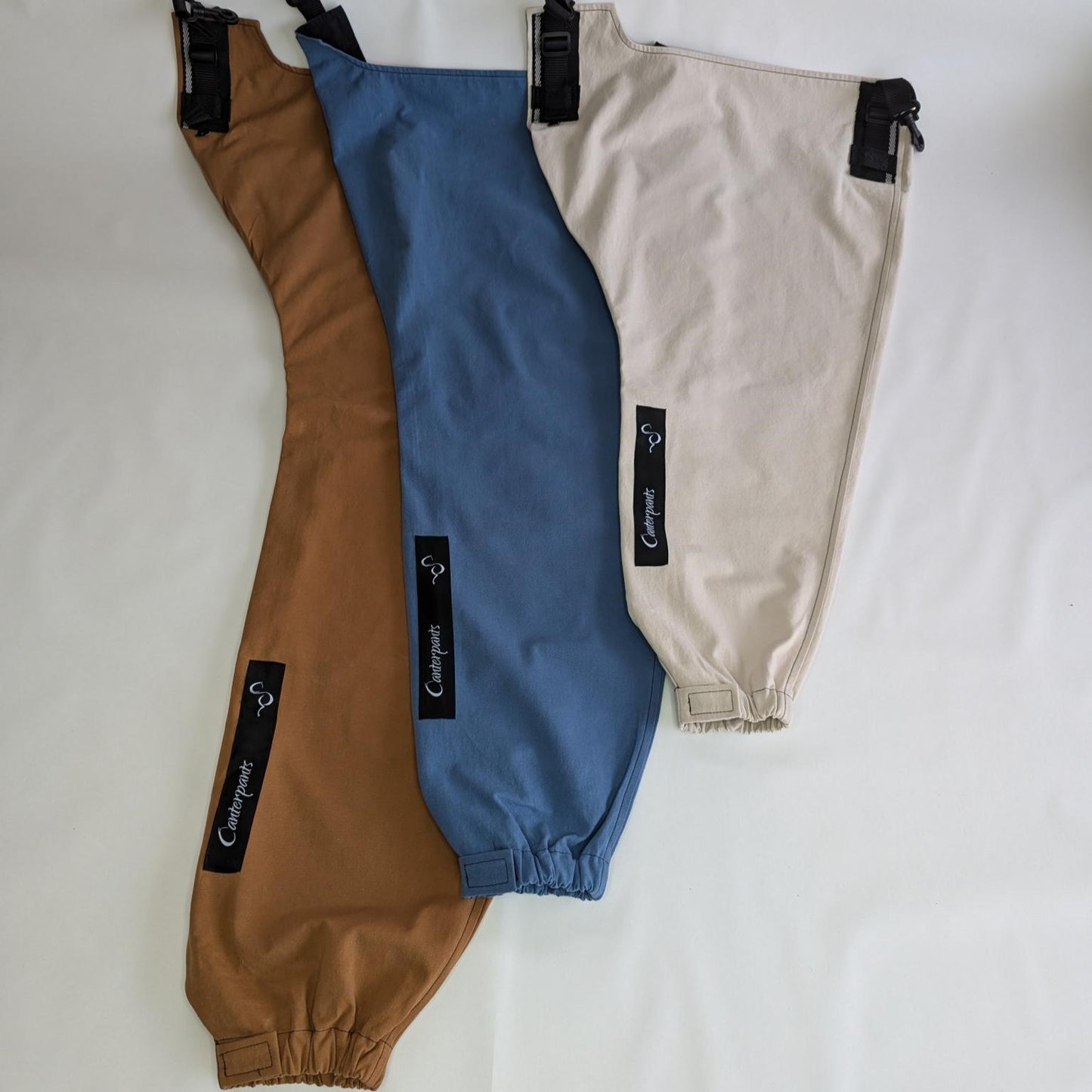 Three front Canterpants legs (large desert brown, medium ocean blue and small beach beige) laid flat on a white background