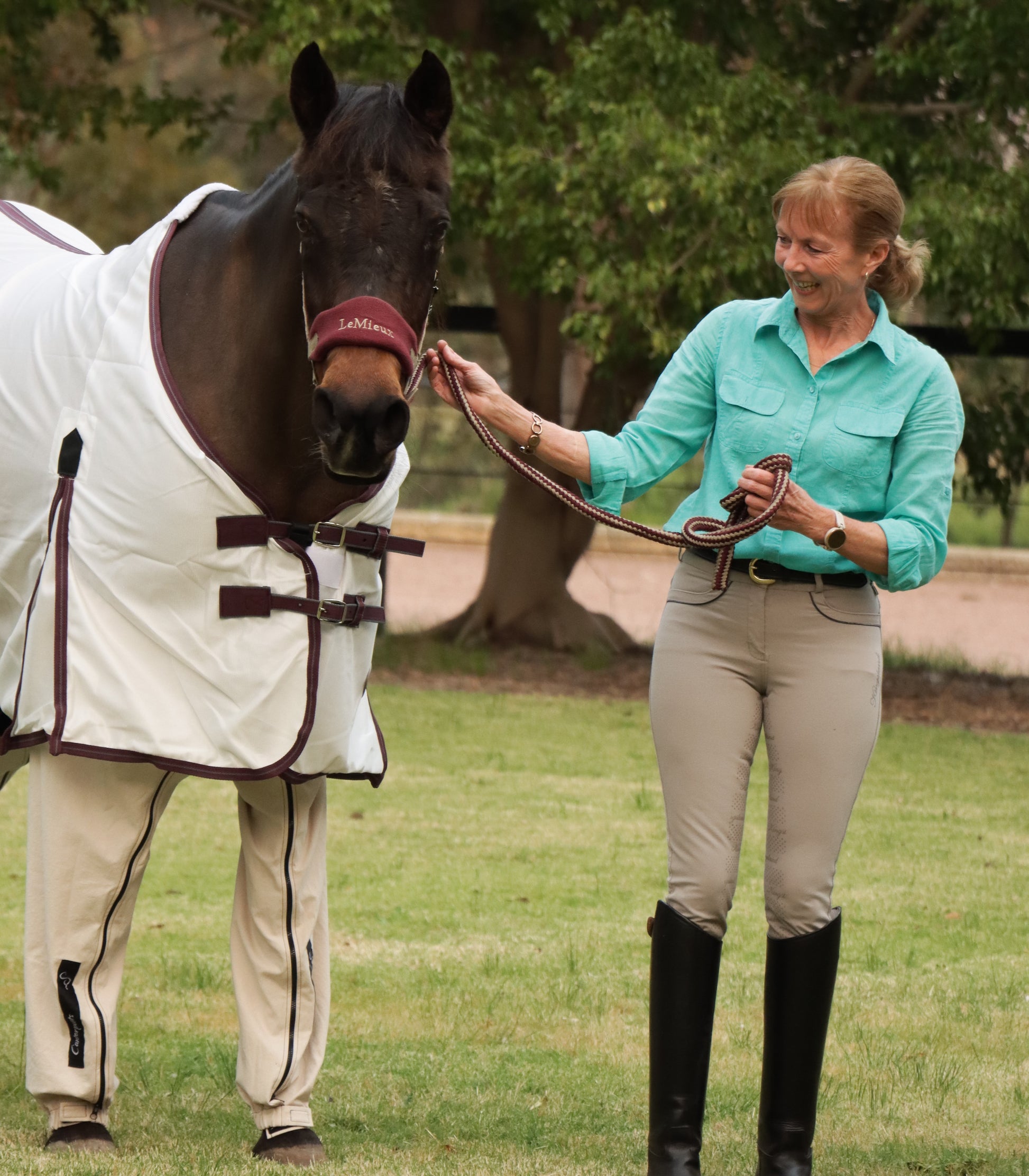 Front view of bay horse (Reena) standing on the lawn wearing beach coloured Canterpants, with founder Yvette